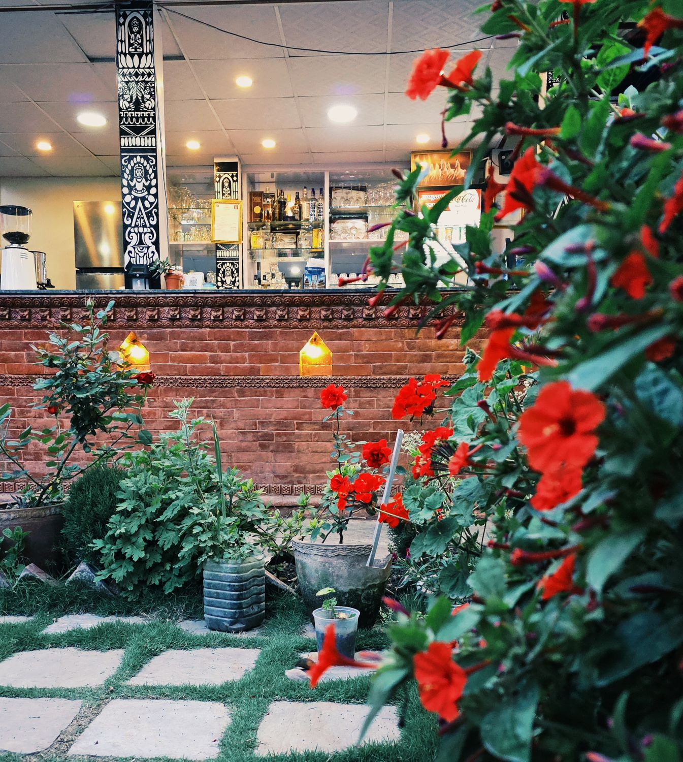 Gwakhancha's courtyard: red geraniums in front of a carved brick bar counter with a black and white mural pillar