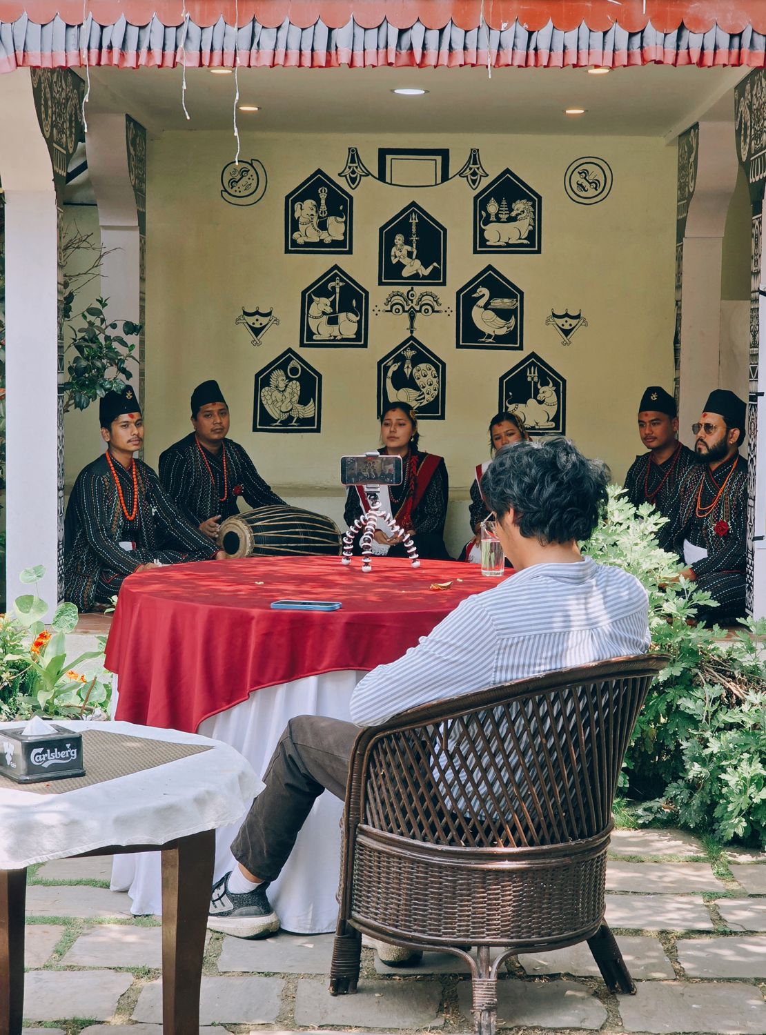 Musicians in traditional Newari dress performing with a dhime drum under the painted courtyard pavilion